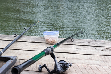 a fishing rod is lying on a wooden pier hanging over the water. on the wooden surface lies bait for fish. Recreation and privacy in nature. Concept for the day of the fisherman. space for text