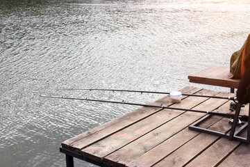 Fototapeta na wymiar a fishing rod is lying on a wooden pier hanging over the water. on the wooden surface lies bait for fish. Recreation and privacy in nature. Concept for the day of the fisherman. space for text