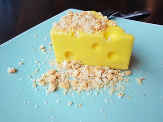 Dessert sweet cake in a sliced cheese shape and crumble on putting on a plate
