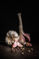 Two heads of garlic and black pepper on a dark background