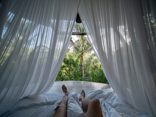 First person view of man: wake up on bed covered with Mosquito net seeing tropical view.