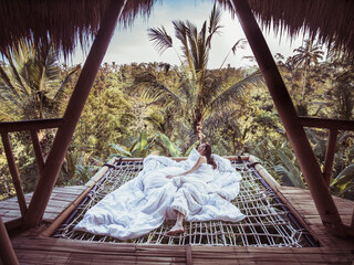 Woman in white blanket on hammock in tree house. Naked woman in morning wakeup. 