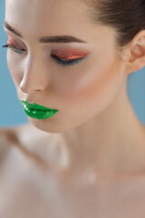 portrait of beautiful naked woman with green lips, pink and blue eyeshadow isolated on blue