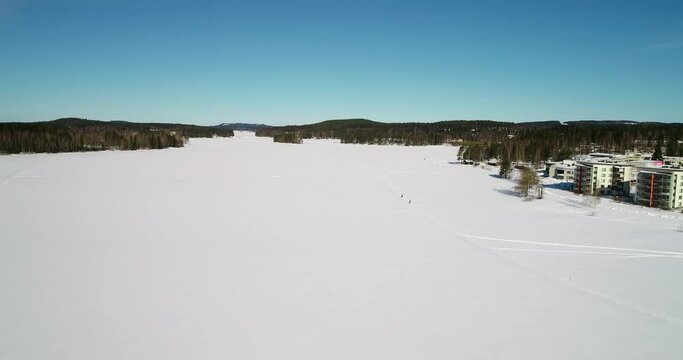 Aerial view towards people on a trail on snow covered ice, at a arctic lake, on a bright and sunny day,in Rovaniemi, Finland - Dolly, drone shot