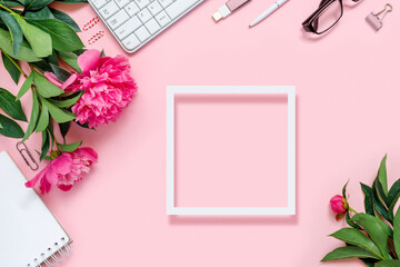 Laptop, accessories and bouquet of beautiful peonies with paper frame, glasses and headphones on pink background.