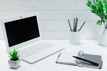 comfortable workplace office - work table with blank white laptop and notebook - home office - designer comfortable workspace - office desk supplies on light background with brick wall