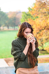 Young girl in nature drinks coffee from paper cup