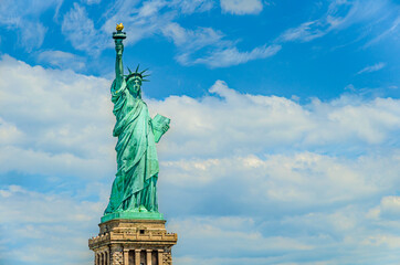 Fototapeta premium The Statue of Liberty designed by Alexandre Gustave Eiffel on a blue sky with white clouds background with 4th of July writing visible on Liberty Island in New York, USA in black and white