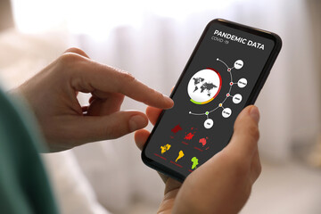 Man with smartphone checking pandemic data indoors, closeup. Coronavirus outbreak