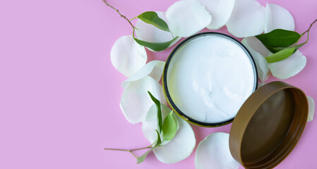 Fototapeta na wymiar an open jar of cosmetic cream and white rose petals on a pink background. cosmetics with the concept of floral style. selective focus.