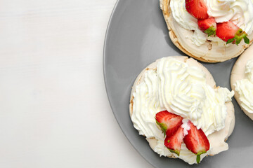 Meringue cakes with strawberry and whipped cream on a grey plate on a green background with copy space. Homemade confectionery. 