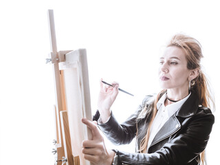 Beautiful girl artist stands in front of easel with a brush on a bright white background. High key...