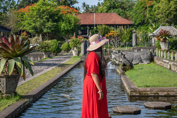A cheerful woman traveller in red dress is standing on the tirtha empul water lake surrounded by fish in Bali