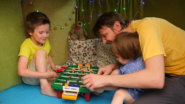 Father with children playing table football indoor. Family spending time at home. Cheerful kids playing with father in the house. Family leisure activity. Quarantine, happy family