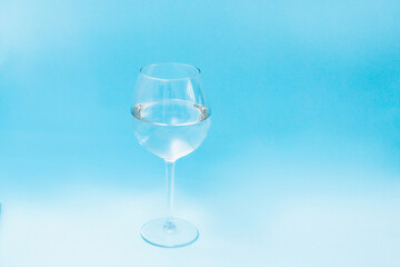 glass wine glass filled with water on a blue background, front view