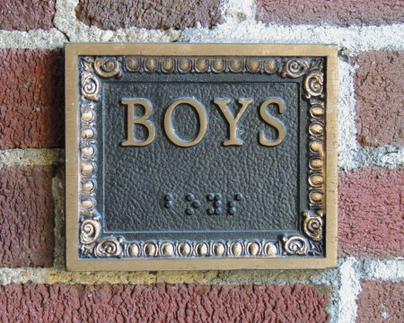 Cartel de ba&ntilde;o publico para ni&ntilde;os de bronce ornamentado con escritura en idioma braile.