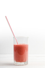Strawberry and banana smoothie in a transparent glass on white wooden table. Copyspace.