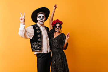 Zombies in mexican attires expressing happiness. Adorable young woman celebrating halloween with friend.