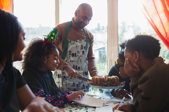 Father serving Christmas cake to family at table