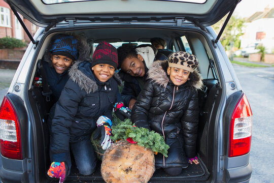 Portrait happy brothers and sister with Christmas tree in back of car