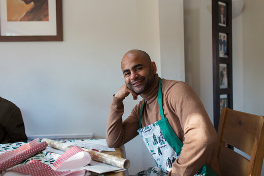 Portrait Happy Man In Christmas Apron Wrapping Gifts At Table