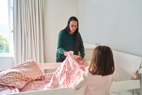 Mother helping daughter make bed