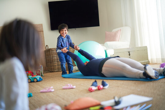 Boy playing with mother exercising on yoga mat in living room