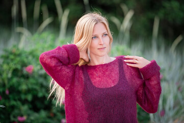 Portrait of a blonde girl who walks outdoors in summer in a thin mohair cherry jumper