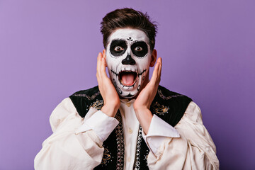 Shocked brown-eyed man screaming on purple background. Handsome male model in zombie costume...