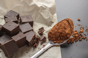 Layout of pieces of dark chocolate and a spoonful of cocoa powder on a black background