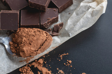 Layout of pieces of dark chocolate and a spoonful of cocoa powder on a black background