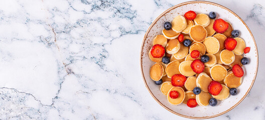 Tiny pancakes with strawberries and blueberries for breakfast.