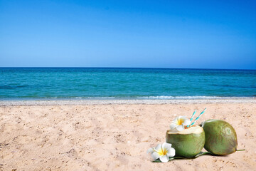 Fototapeta na wymiar Green coconuts with refreshing drink and beautiful flowers on sandy beach near sea, space for text