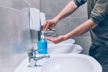 A young man washing his hands with liquid soap in the toilet, on the background of the washbasin. Stop COVID-19