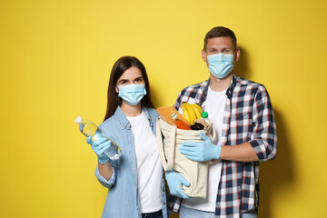 Volunteers in protective masks and gloves with products on yellow background. Aid during...