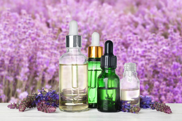 Bottles of essential oils and wildflowers on wooden table against blurred background