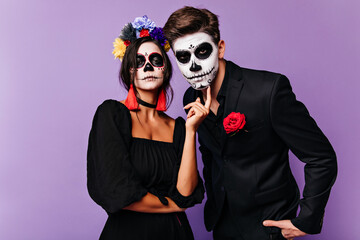 Serious girl in masquerade costume posing on purple background. Funny couple in carnival attires looking to camera.