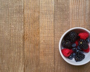 raspberries, blueberries, and blackberries stand in a bowl on a wooden board