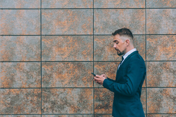 Businessman in a blue jacket with a smartphone in his hand on a wall background.