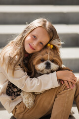 A cute smiling blonde girl of 9 years old gently hugs a dog.