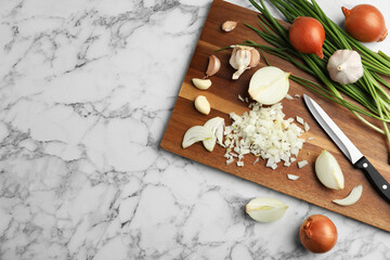Board with cut onion and garlic on marble table, top view. Space for text