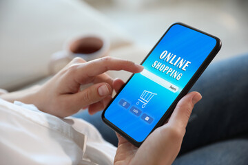 Woman holding smartphone with online shopping website on screen indoors, closeup