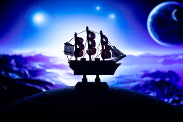 Beautiful boat toy over a blue balll with blurred violet stars, crescent mooon and a tree at...