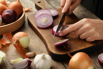 Woman cutting red onion on wooden board, closeup