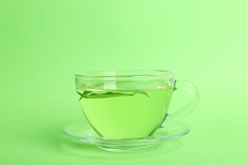 Cup of aromatic green tea with leaves on color background