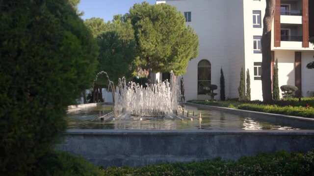 Beautiful fountain with flowing water. A white house and green trees in the background. 