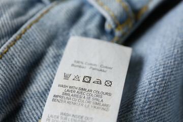 Clothing label with care symbols and material content on blue jeans, closeup view