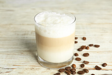 Delicious latte macchiato and coffee beans on white wooden table