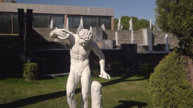 A white statue in the background of decorative fountain. Water flows over large artificial stones. Landscape design. 