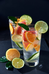 Health care, fitness, healthy nutrition diet concept. Fresh cool homemade citrus infused detox water with grapefruit, orange, lemon and lime and ice in glasses on dark background.